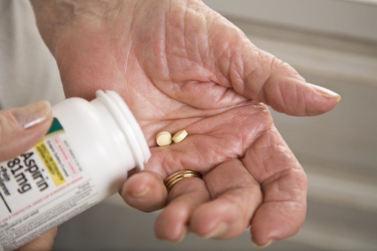 closeup of a senior person's hands taking two aspirin from the bottle