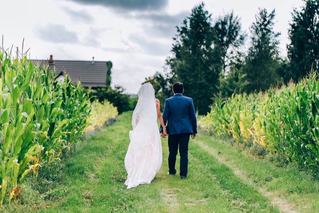 bride and groom walking through cornfield This Is the Age Most People Get Married in Every U.S. State