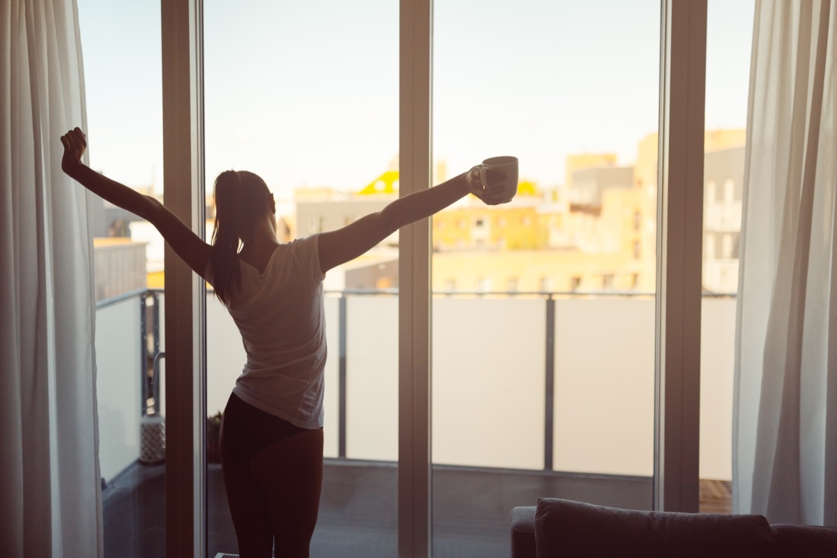 woman stretching in front of window with coffee