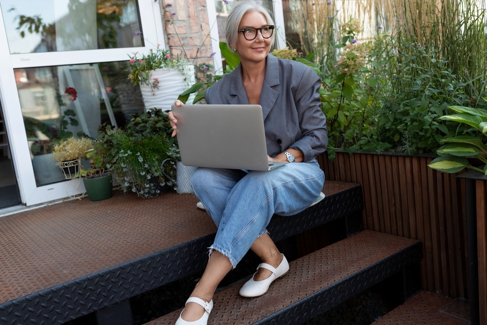 Stylish senior woman in blazer and jeans on laptop working from home