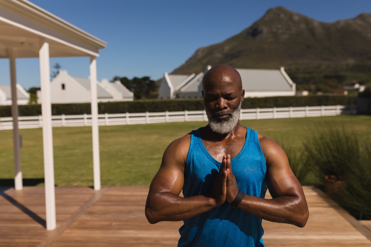 Older black man doing yoga in his backyard