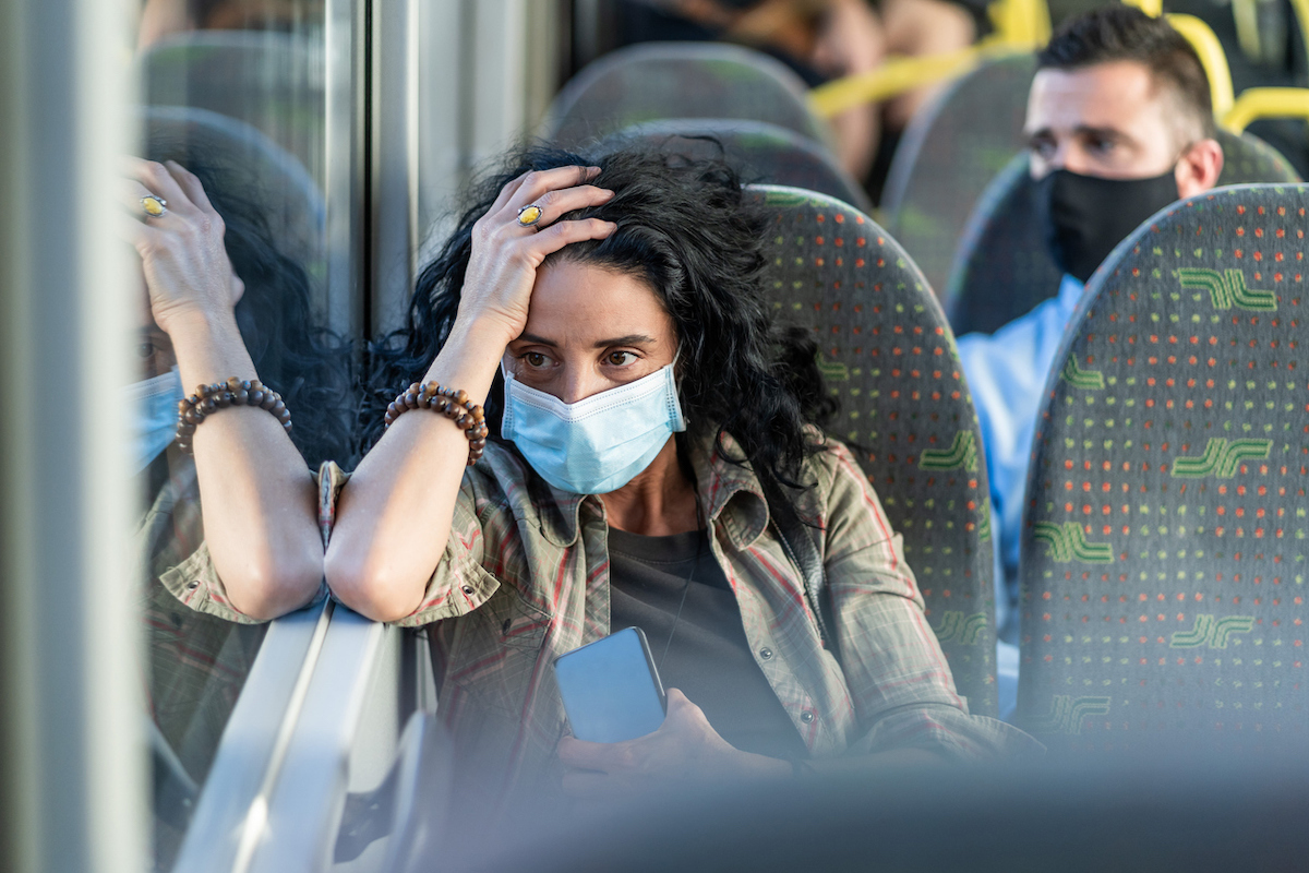 Woman with a protective face mask to avoid infectious diseases, looking tired while traveling by bus