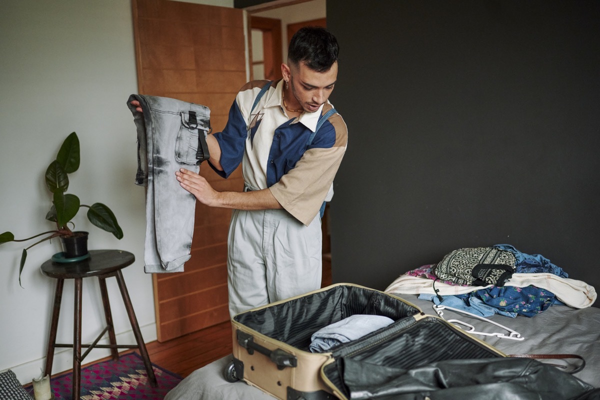 Young man in a bedroom packing and organising clothing for a trip into a suitcase