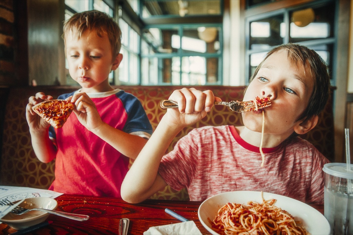 Little boys eating pasta and pizza in restaurant