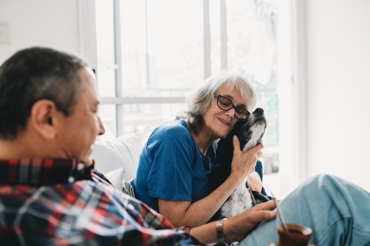 Mature couple spending time together with their dog at home. They are sitting on the sofa, drinking yerba mate together