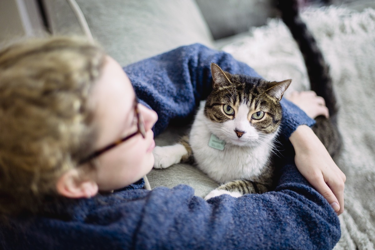 a girl wearing eyeglasses with her arms around her tabby cat