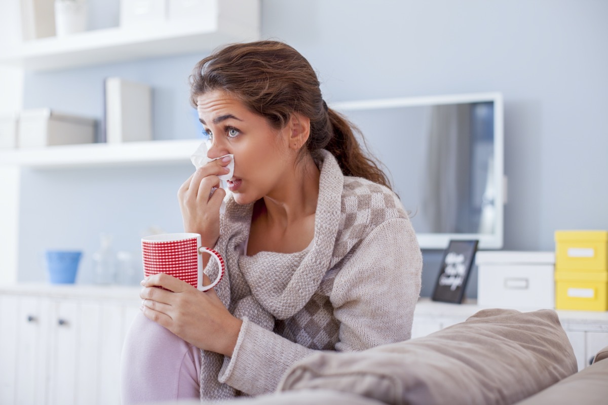 Sick woman blowing nose on her sofa.