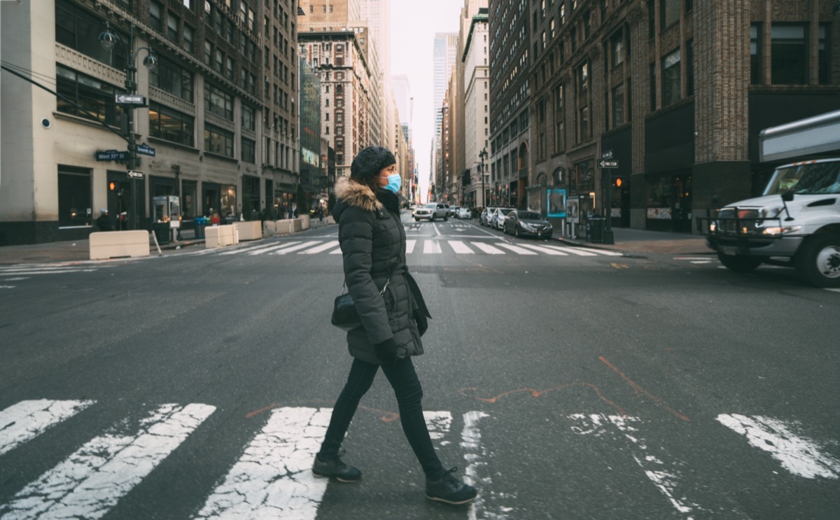 Woman wearing surgical mask going through crosswalk in midtown manhattan.Concept of Coronavirus, COVID-19 and quarantine