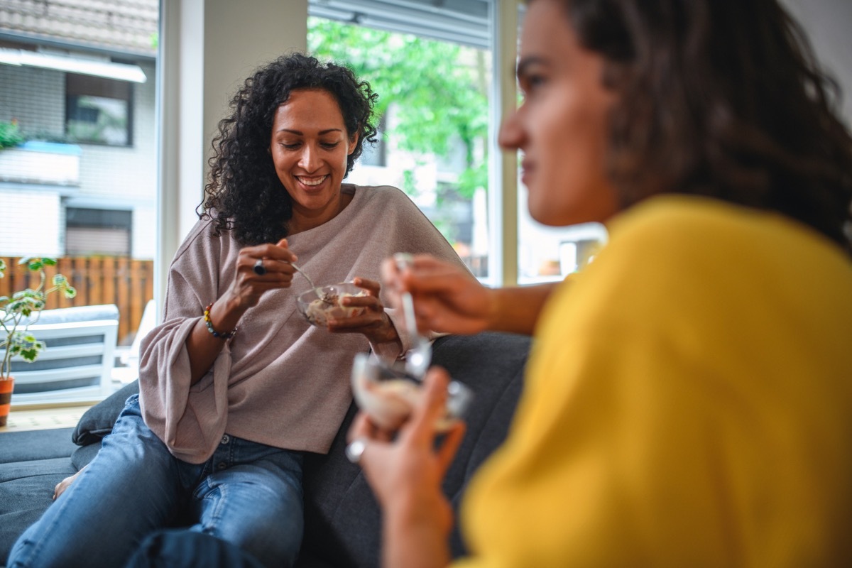 mother and son eating ice cream indoors in a living room on a sofa together. They are having a discussion.