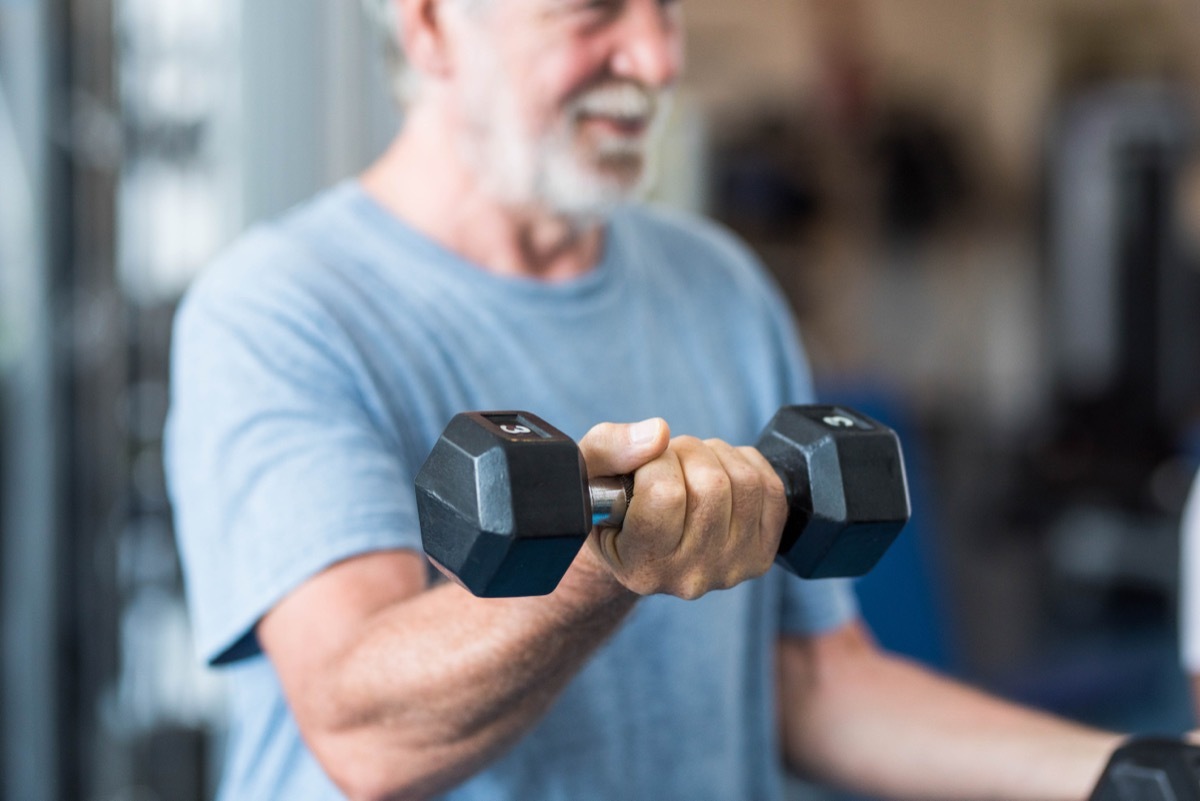 close up of mature man holding two dumbbells doing exercise at the gym to be healthy and fitness - portrait of active senior lifting weight