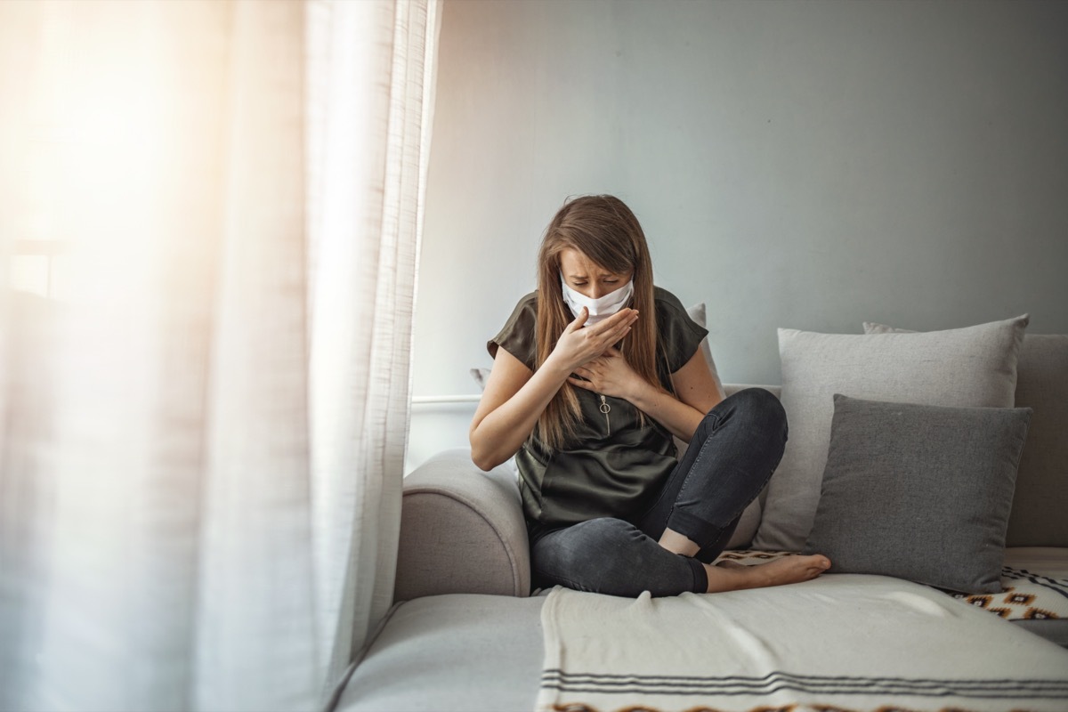 Woman wearing surgical mask on face protective for spreading of disease Covid-19 pandemic.. Girl symptom cough while sitting on Sofa.