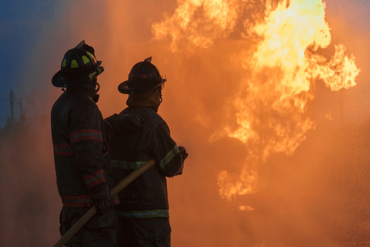 Side view of Firefighter spraying high pressure water to control fire at Night.