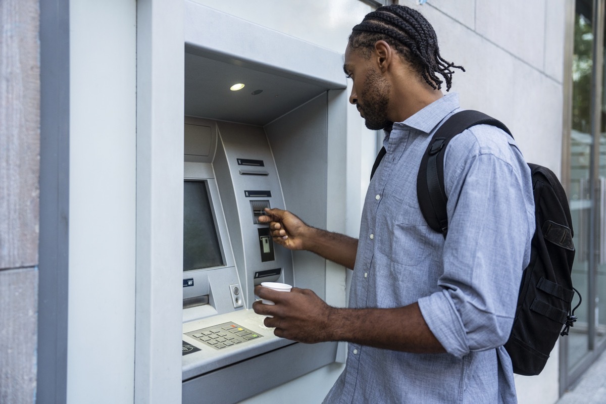 man taking out bank card after using ATM while standing on street during daytime