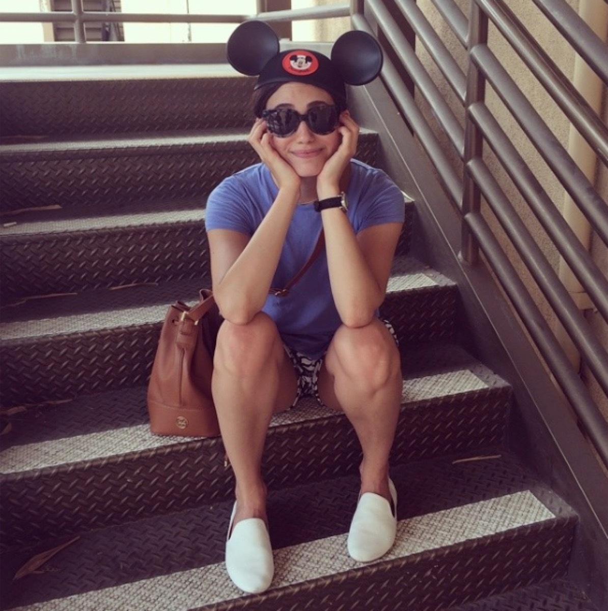 emmy rossum sitting on stairs wearing disney hat