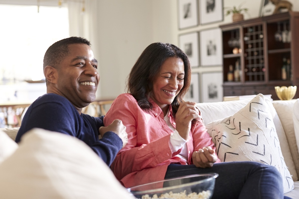 middle aged black couple laughing and eating popcorn on the couch