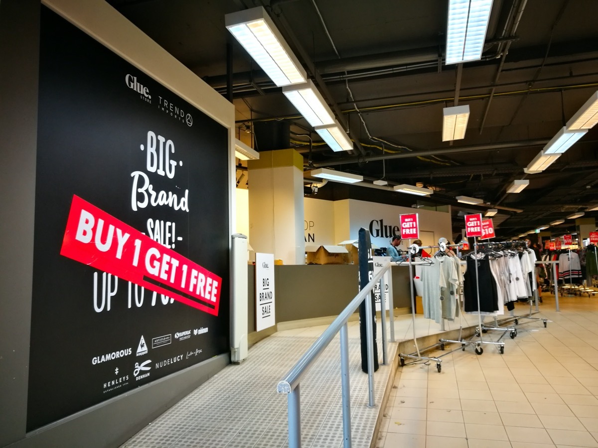 'Buy 1 Get 1 Free' Sign on wall of store and rack of clothes on sale