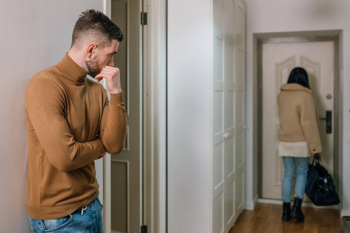 Young man watching sadly as his girlfriend walks out the door.