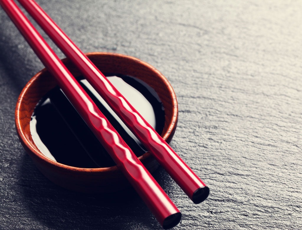 red chopsticks and bowl of soy sauce on dark background