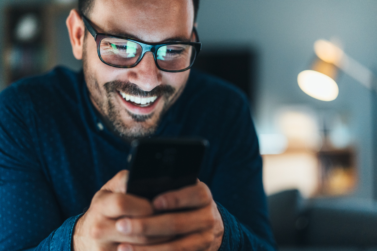 Young man wearing glasses and laughing while looking at jokes on his phone