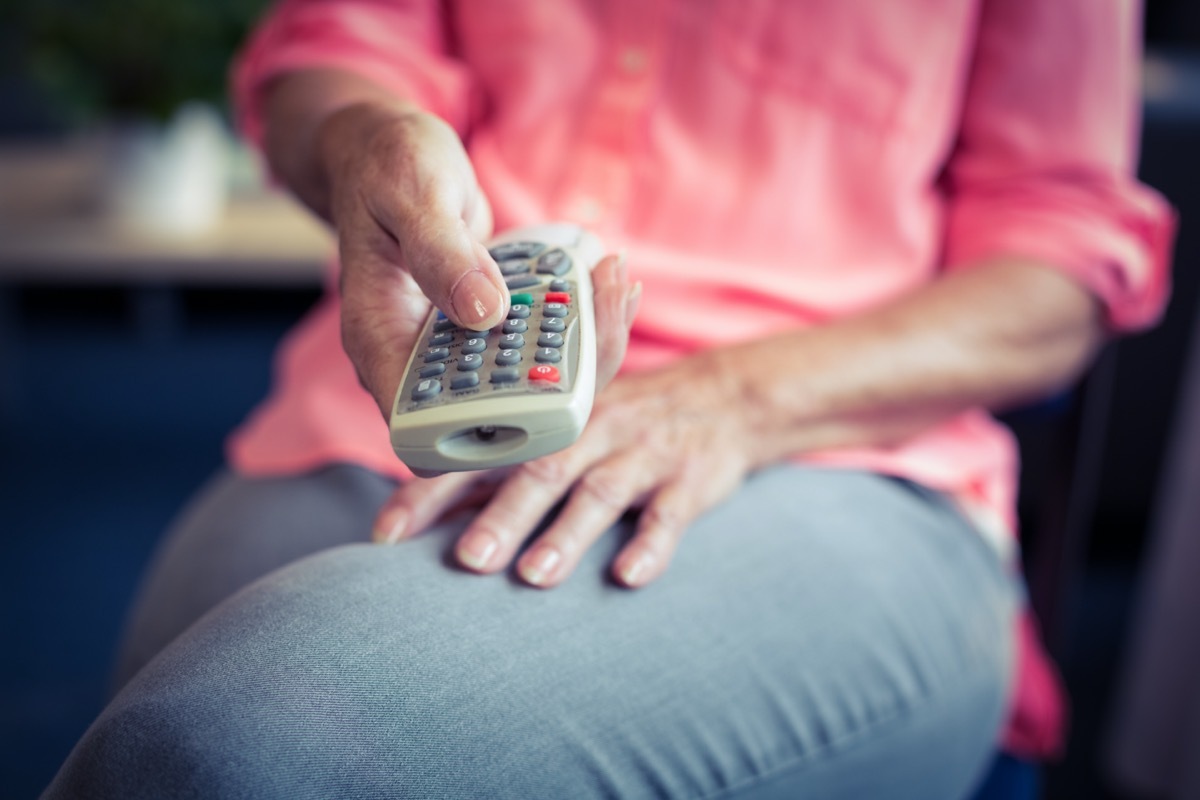 Senior woman changing tv channel at home